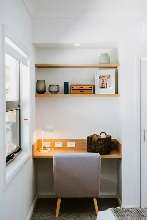 Un pequeño rincón de escritorio con estantes, una silla y una ventana.