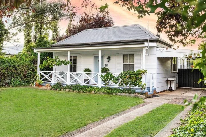Una casa blanca con una galería al frente y césped verde.
