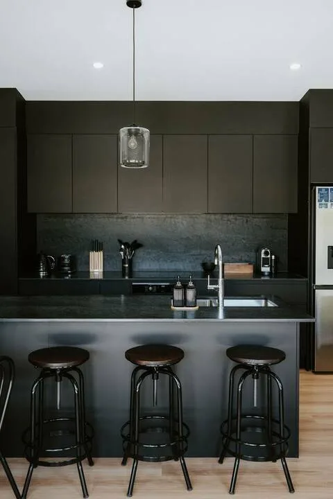 Una cocina moderna con una isla oscura y taburetes.