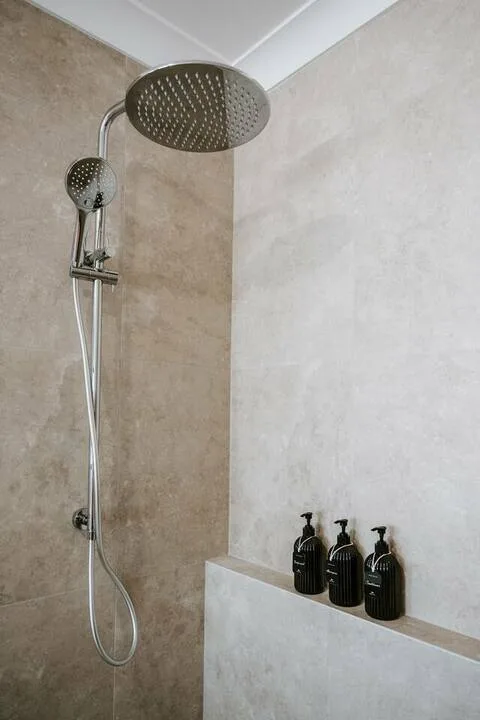 Una ducha con azulejos, una alcachofa superior grande y una ducha de mano.