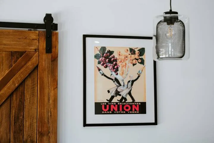 Una pared con un cartel enmarcado de vino, una lámpara colgante y una puerta corrediza de madera.