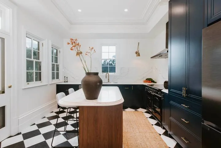 Una cocina luminosa con una isla central, gabinetes oscuros y suelo de cuadros blancos y negros.