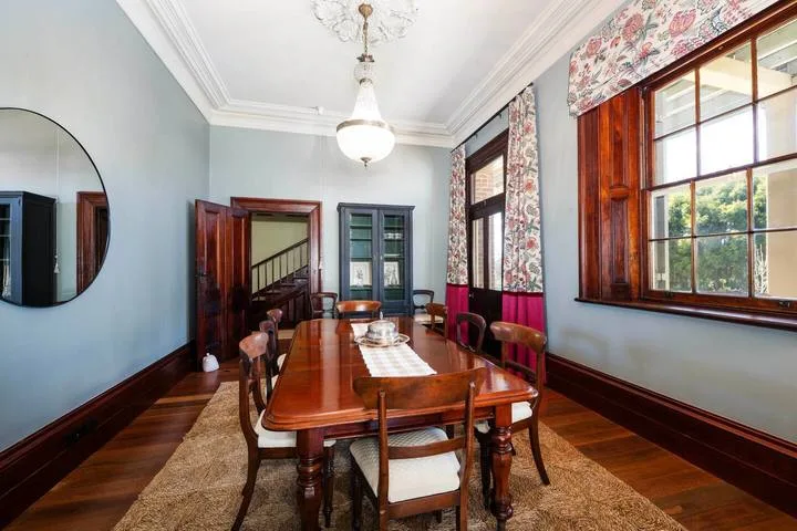Un comedor con una mesa larga de madera, sillas y ventanas grandes.