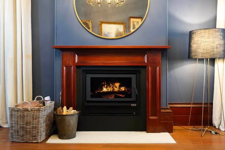 Una chimenea en una sala de estar está debajo de un espejo redondo, con una lámpara de pie cerca.