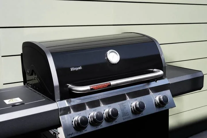 Una parrilla exterior con tapa, indicador de temperatura y perillas de control.