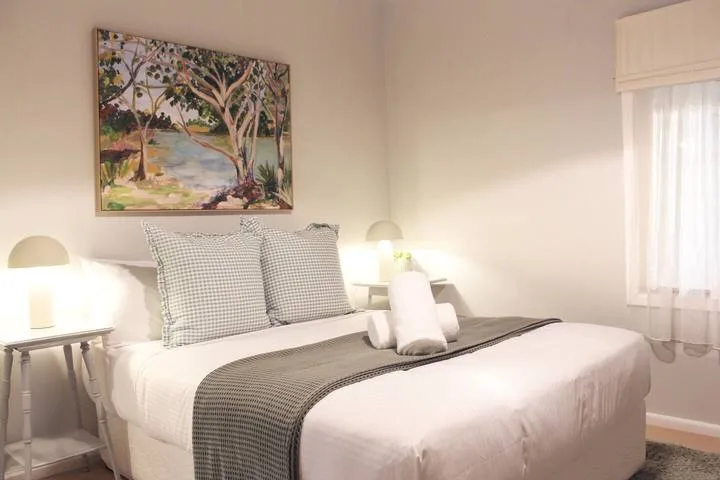 Un dormitorio con una cama bien tendida y un cuadro de paisaje enmarcado encima.