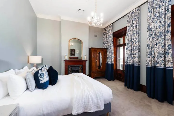 Un dormitorio luminoso con una cama grande, cortinas estampadas y un armario de madera.