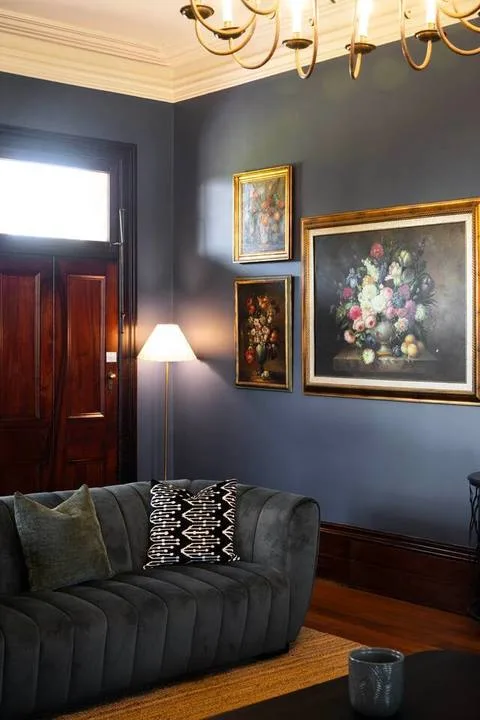 Una sala de estar oscura con un sofá curvo y cuadros florales enmarcados.