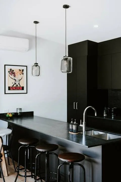 Una cocina moderna con una isla oscura, asientos de barra y lámparas colgantes.