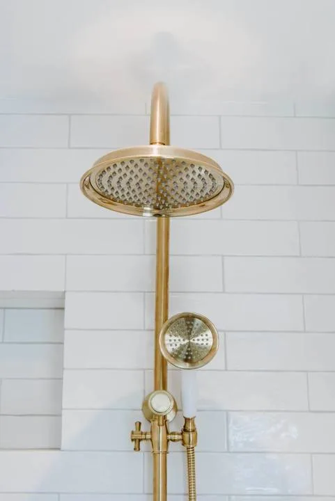 Un accesorio de ducha dorado está montado sobre una pared de azulejos blancos.