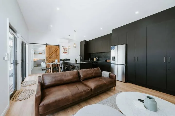 Una sala de estar con un sofá marrón y una cocina abierta al fondo.