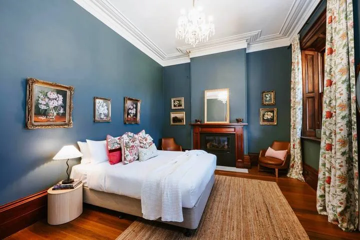 Un dormitorio con una cama blanca, paredes azules y una chimenea.