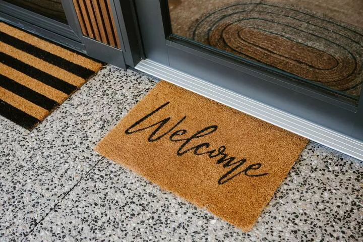 Una entrada con un felpudo de bienvenida junto a una puerta de vidrio.