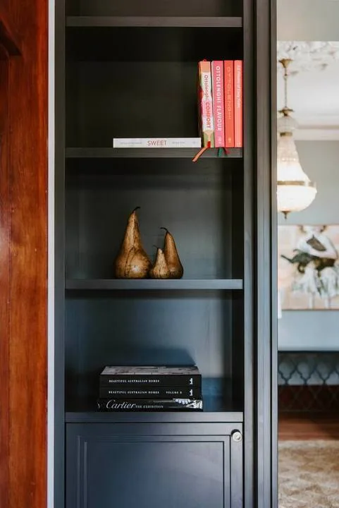 Una estantería empotrada oscura exhibe libros y objetos decorativos.