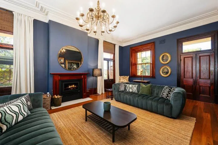 Una sala de estar con paredes azul oscuro, asientos verdes y una chimenea.