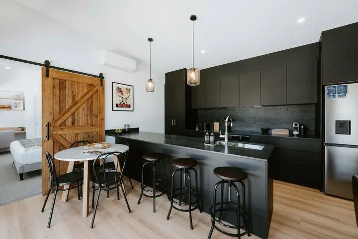 Una cocina moderna con una isla larga y gabinetes oscuros se abre a un comedor.