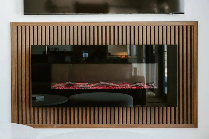 Una chimenea moderna está empotrada en una pared de listones de madera, bajo un televisor.