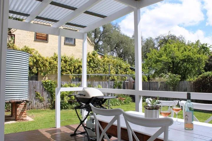 Un patio exterior cubierto tiene una mesa de comedor junto a un jardín.