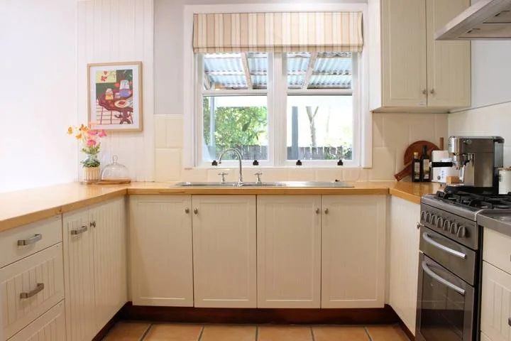 Una cocina luminosa con un fregadero bajo una ventana y una estufa junto a la encimera.