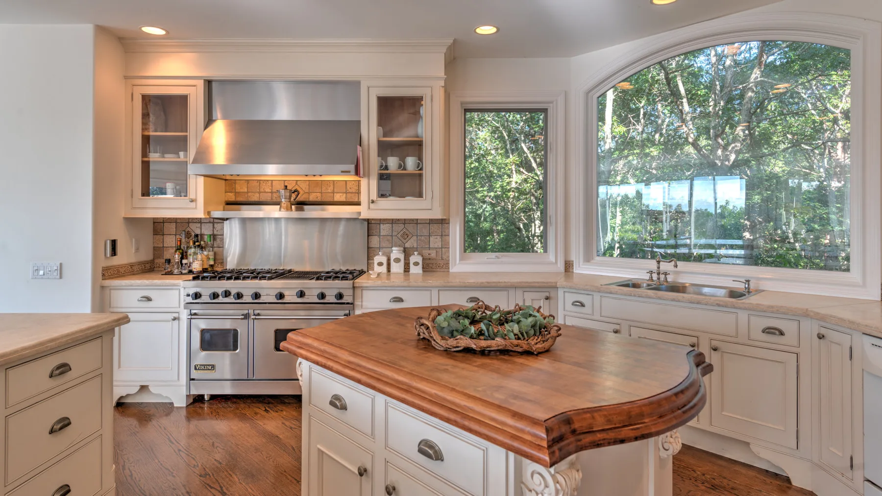 Una cocina luminosa con una gran isla de madera y una amplia ventana con vista a los árboles.