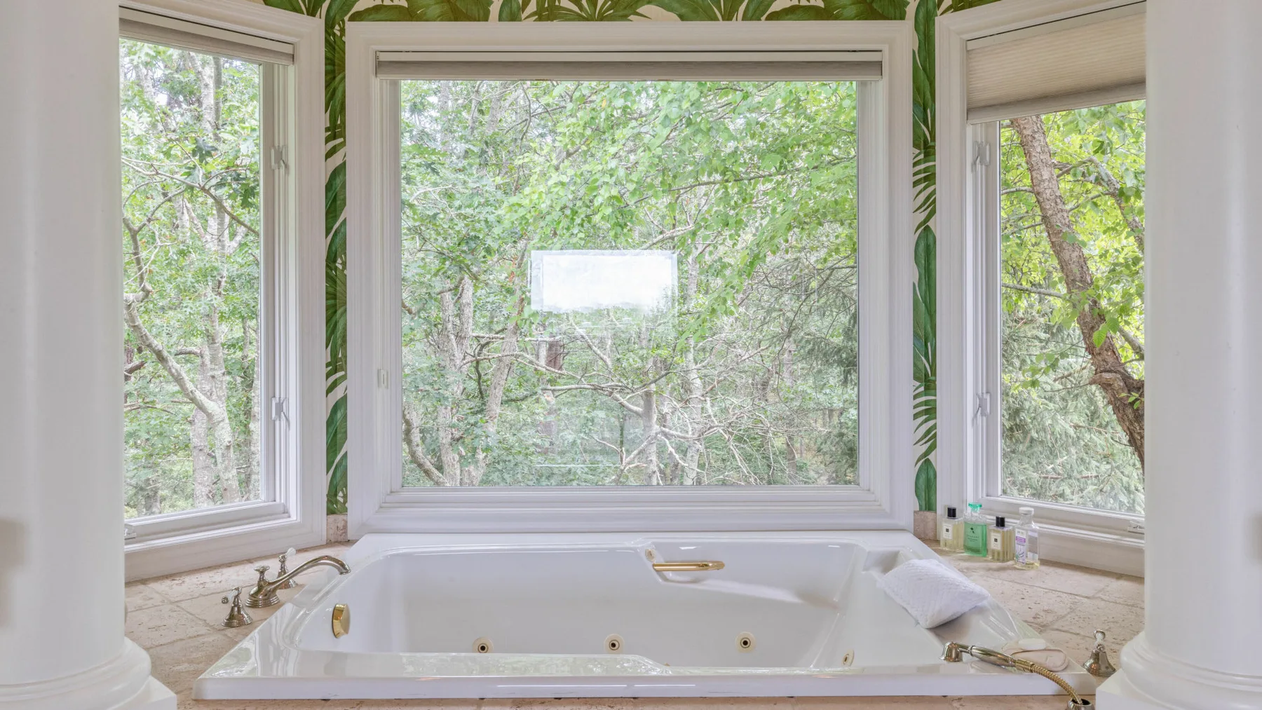 Una bañera está bajo amplias ventanas con vistas a árboles frondosos.