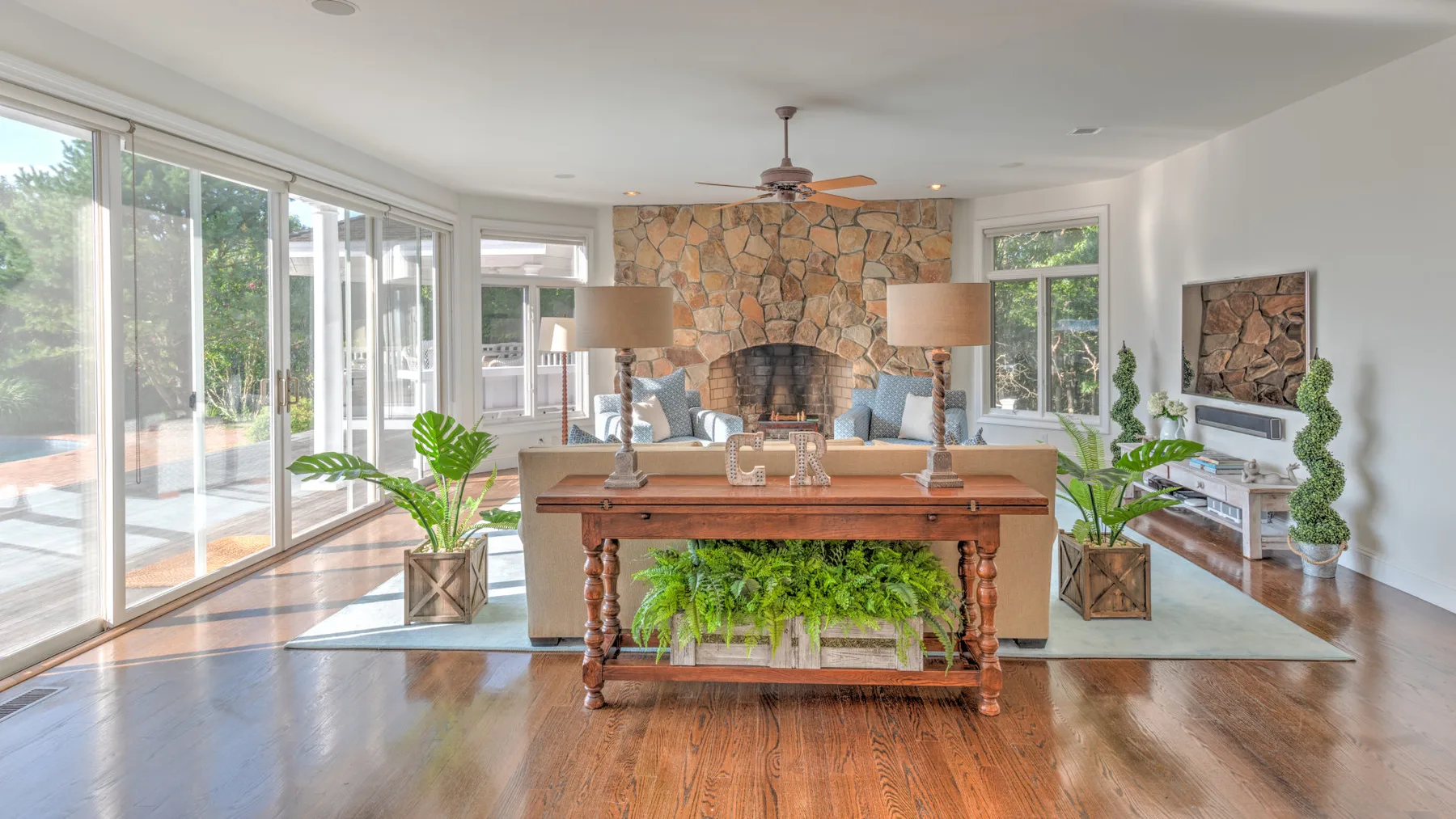Una sala luminosa con chimenea de piedra, grandes ventanas y una mesa de madera.