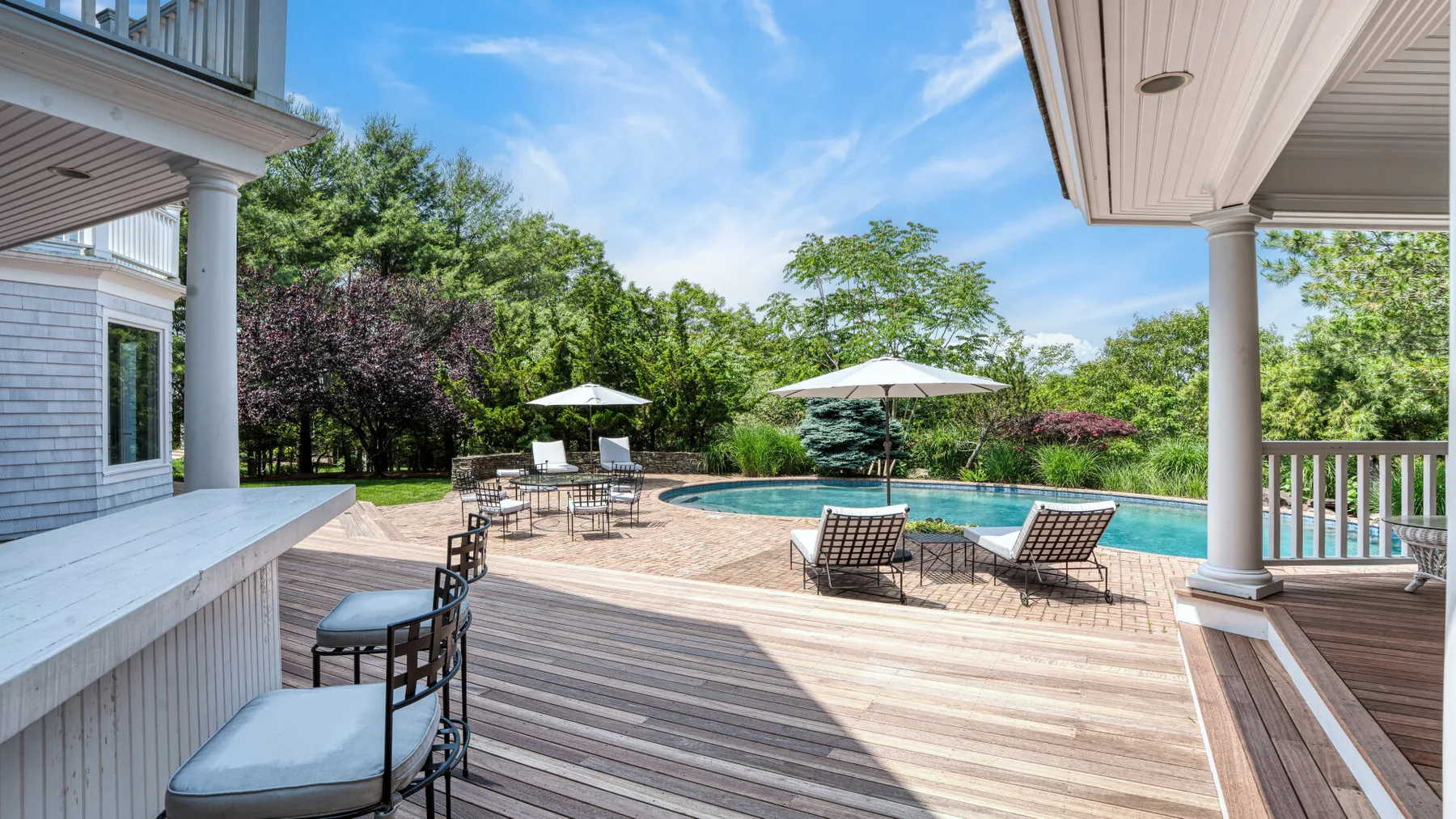 Una terraza trasera con piscina, asientos de patio y árboles.