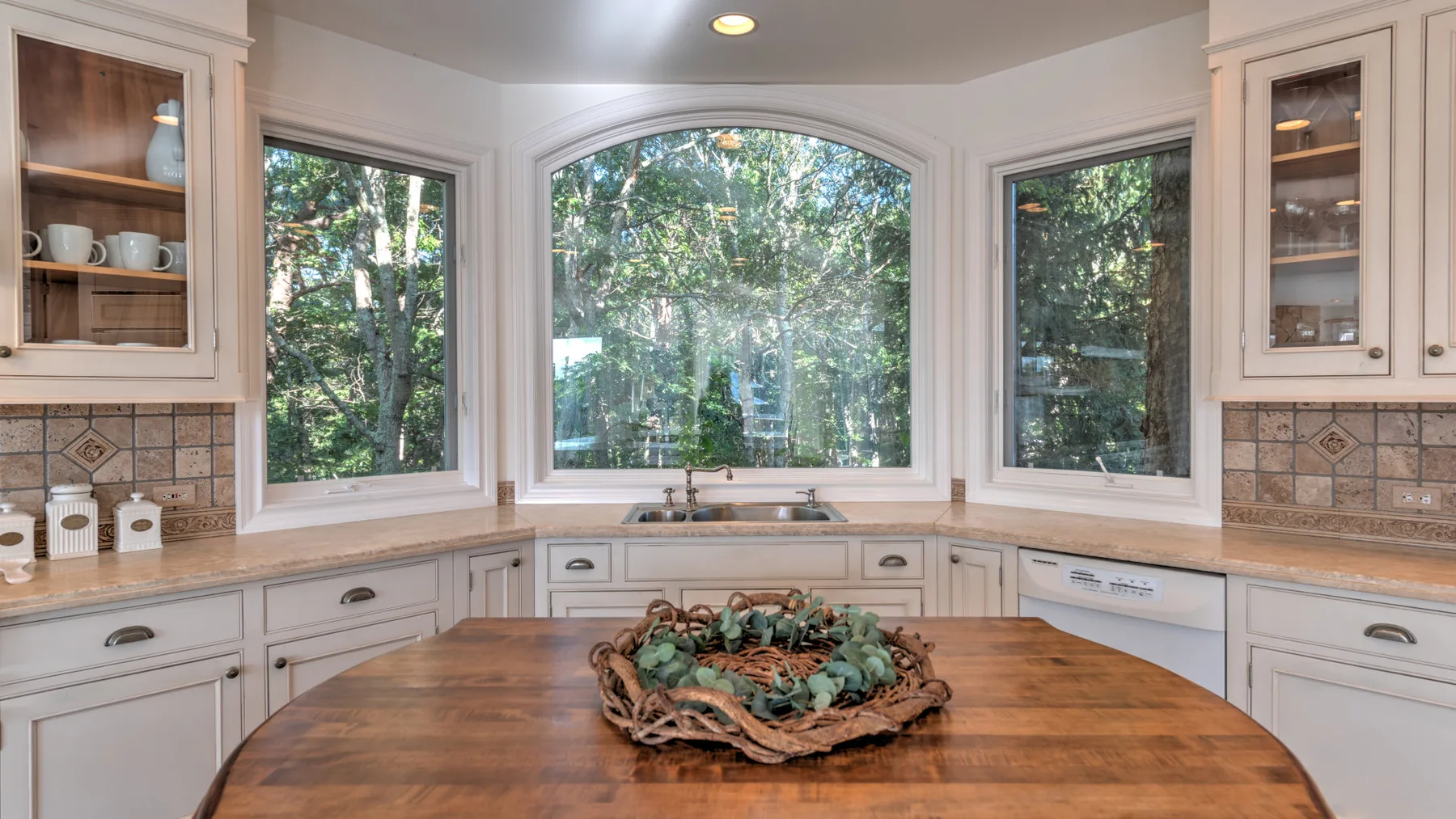 Una cocina luminosa con una gran isla de madera y amplias ventanas con vistas a los árboles.