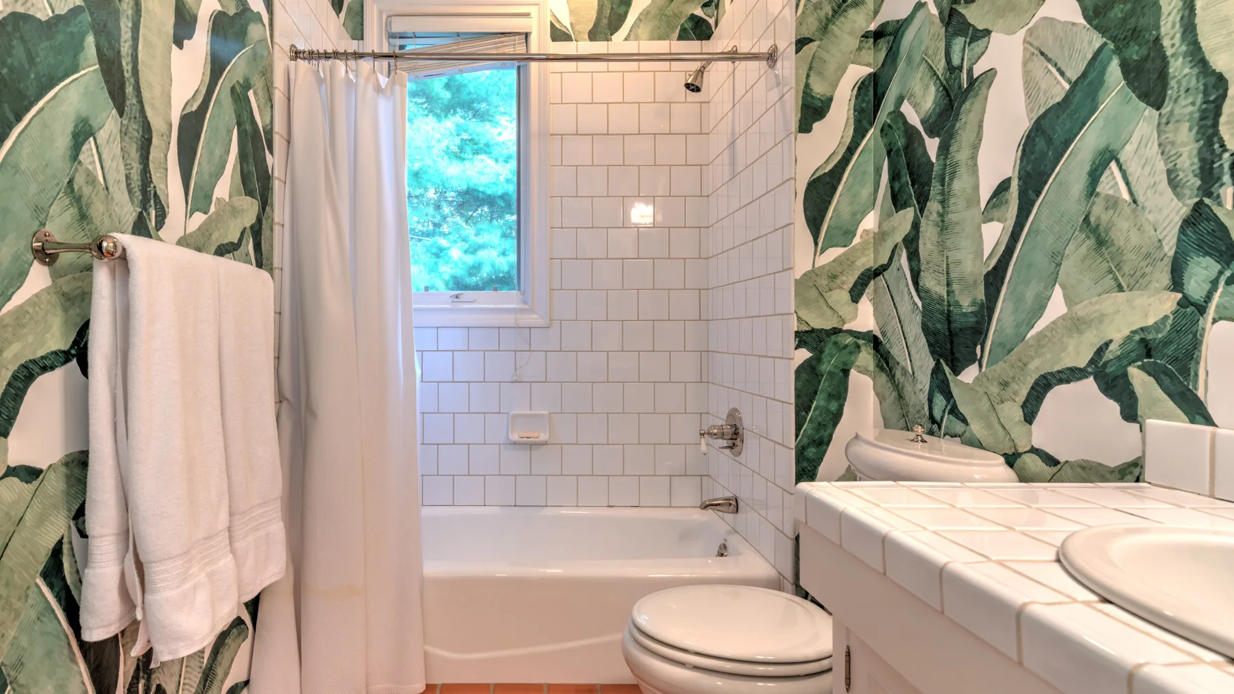 Un baño con bañera alicatada, ducha y un revestimiento de pared con hojas.
