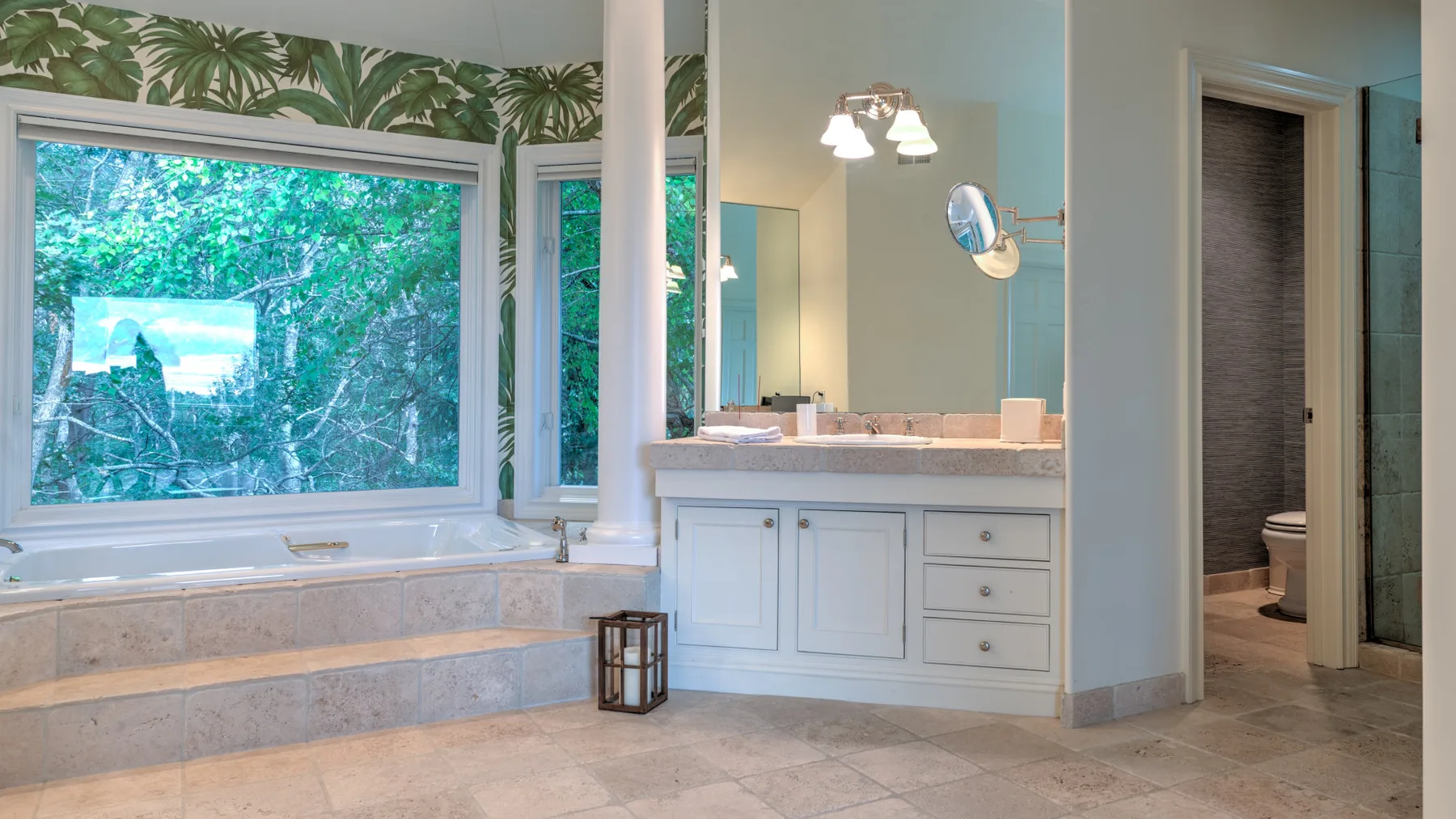 Un baño con bañera empotrada, lavabo y ventanas con vistas a la vegetación.