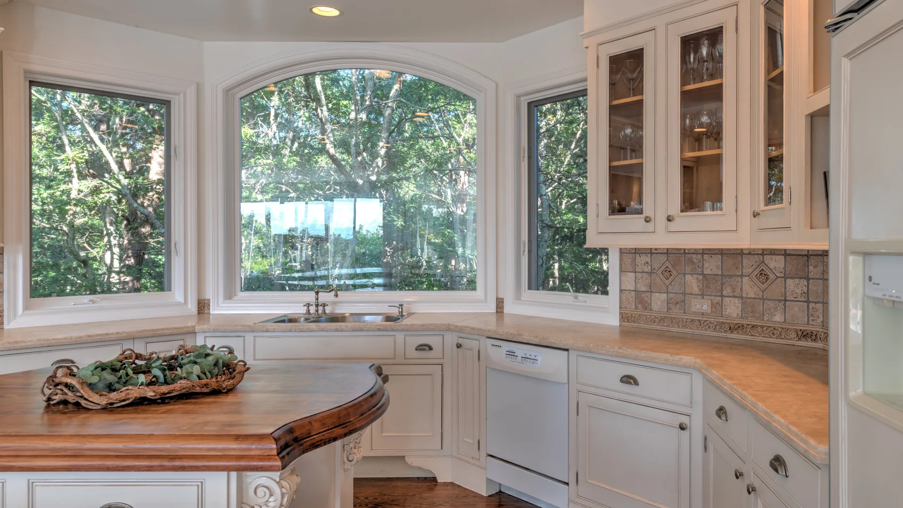 Una cocina luminosa con gabinetes blancos, una isla curva y grandes ventanas.