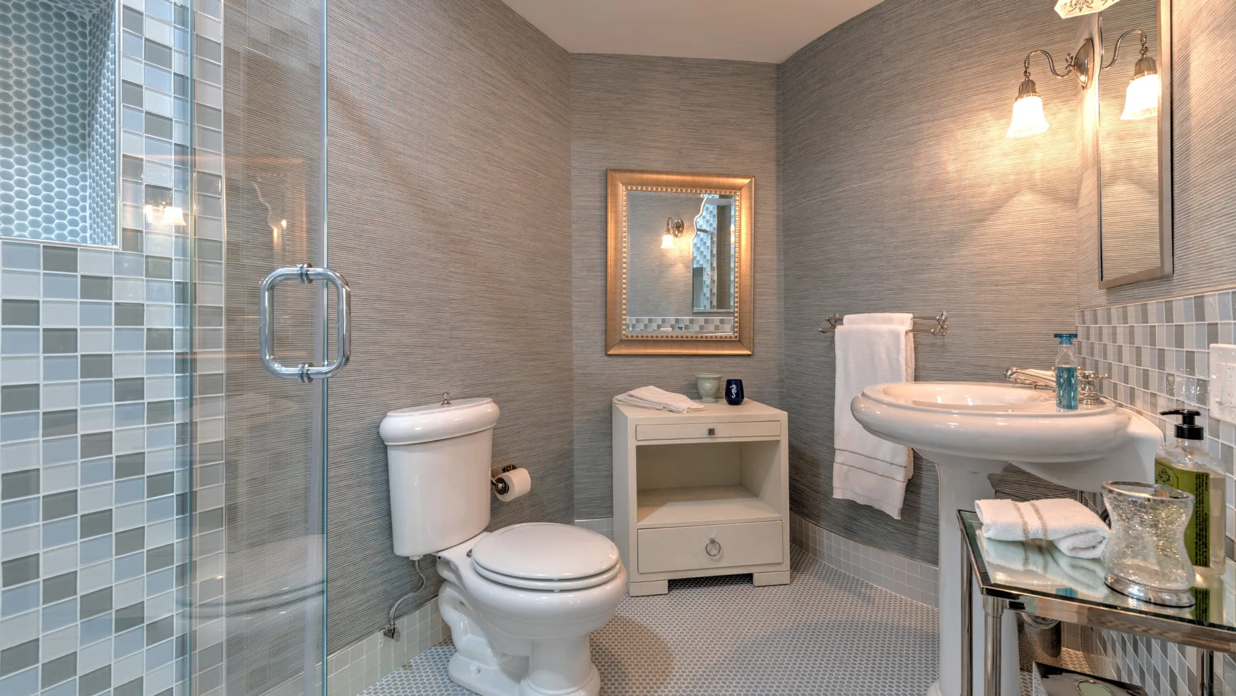 Un baño con azulejos, ducha de vidrio, inodoro y lavabo.