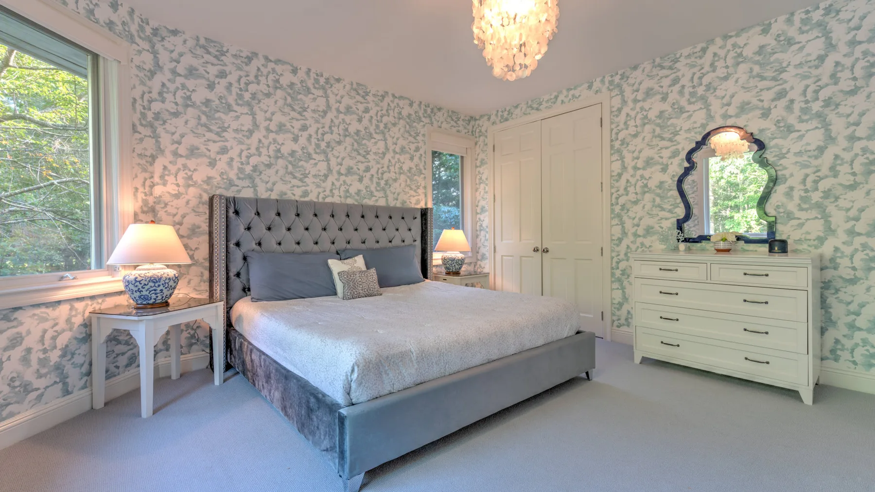 Un dormitorio con una cama, papel tapiz estampado y una cómoda.
