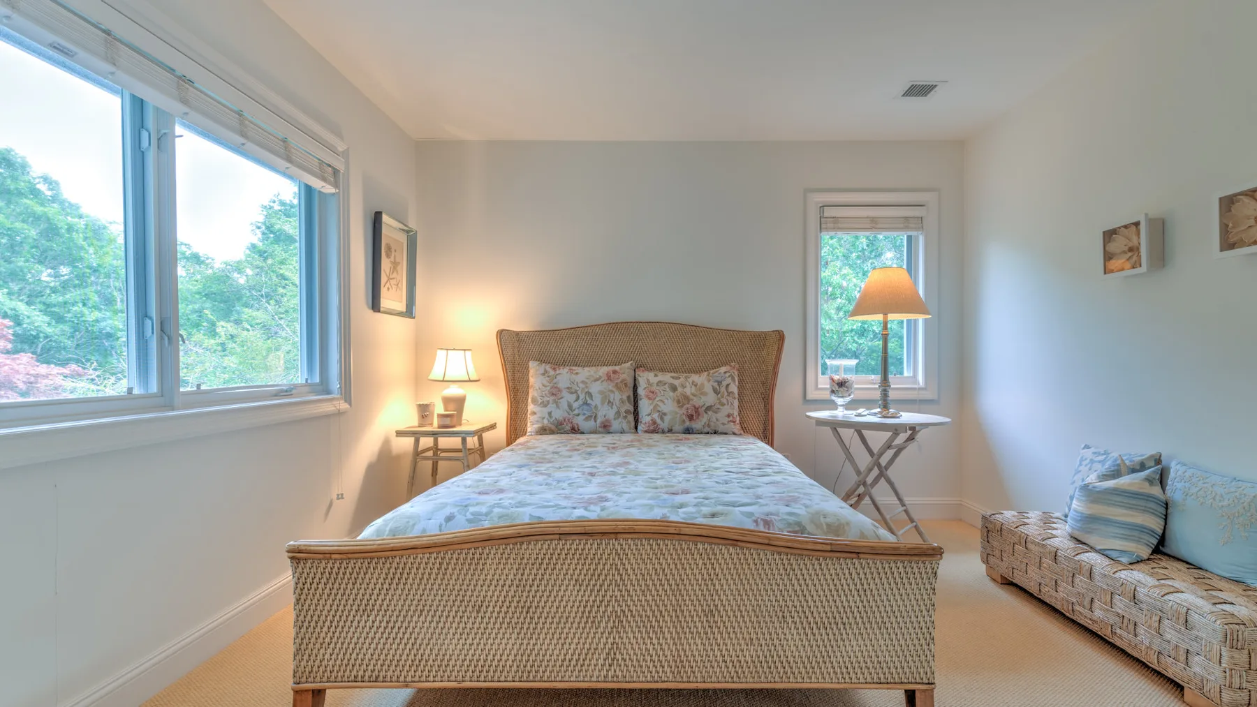 Un dormitorio luminoso con una cama de tejido trenzado y grandes ventanas con vistas a los árboles.