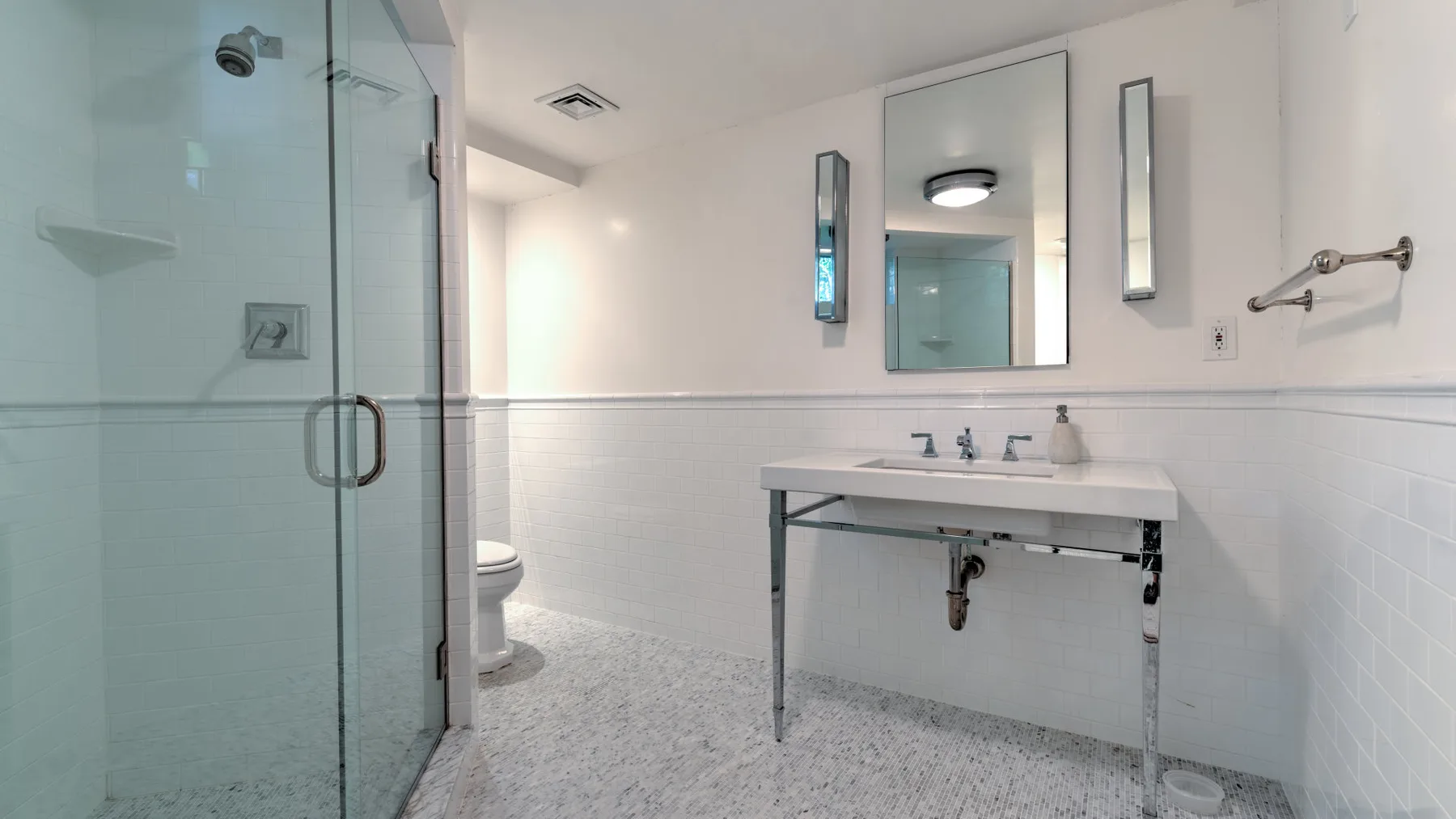 Un baño con ducha de vidrio, espejo de pared y lavabo abierto.