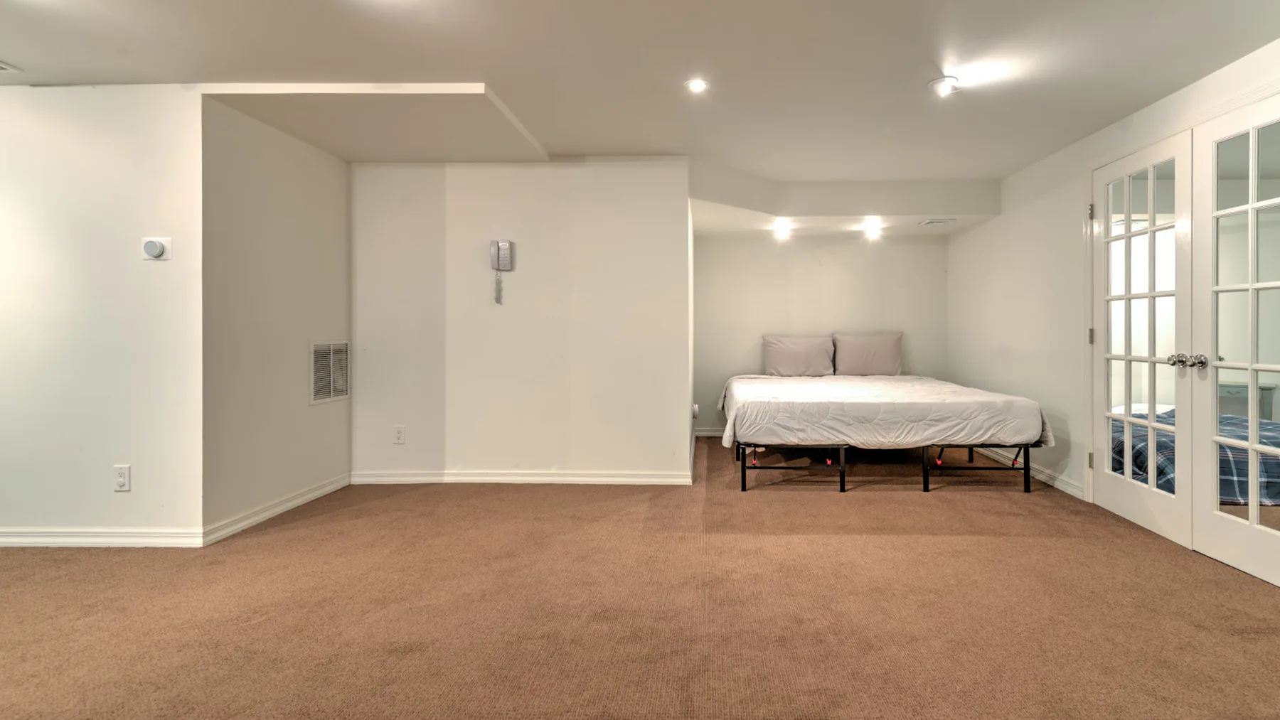 Un dormitorio alfombrado con una cama y puertas con paneles de vidrio.