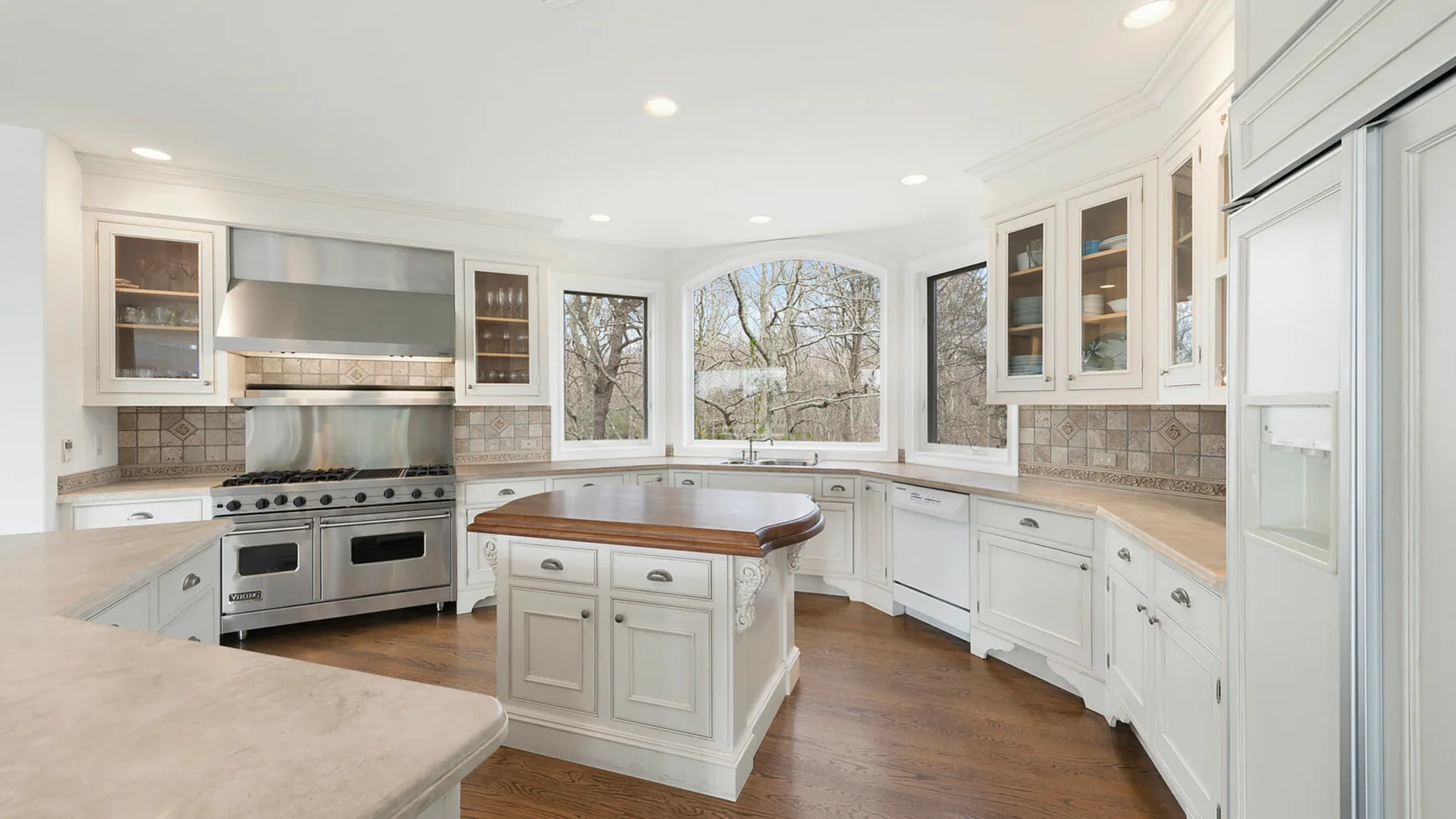 Una cocina luminosa con gabinetes blancos, una isla central y grandes ventanas.