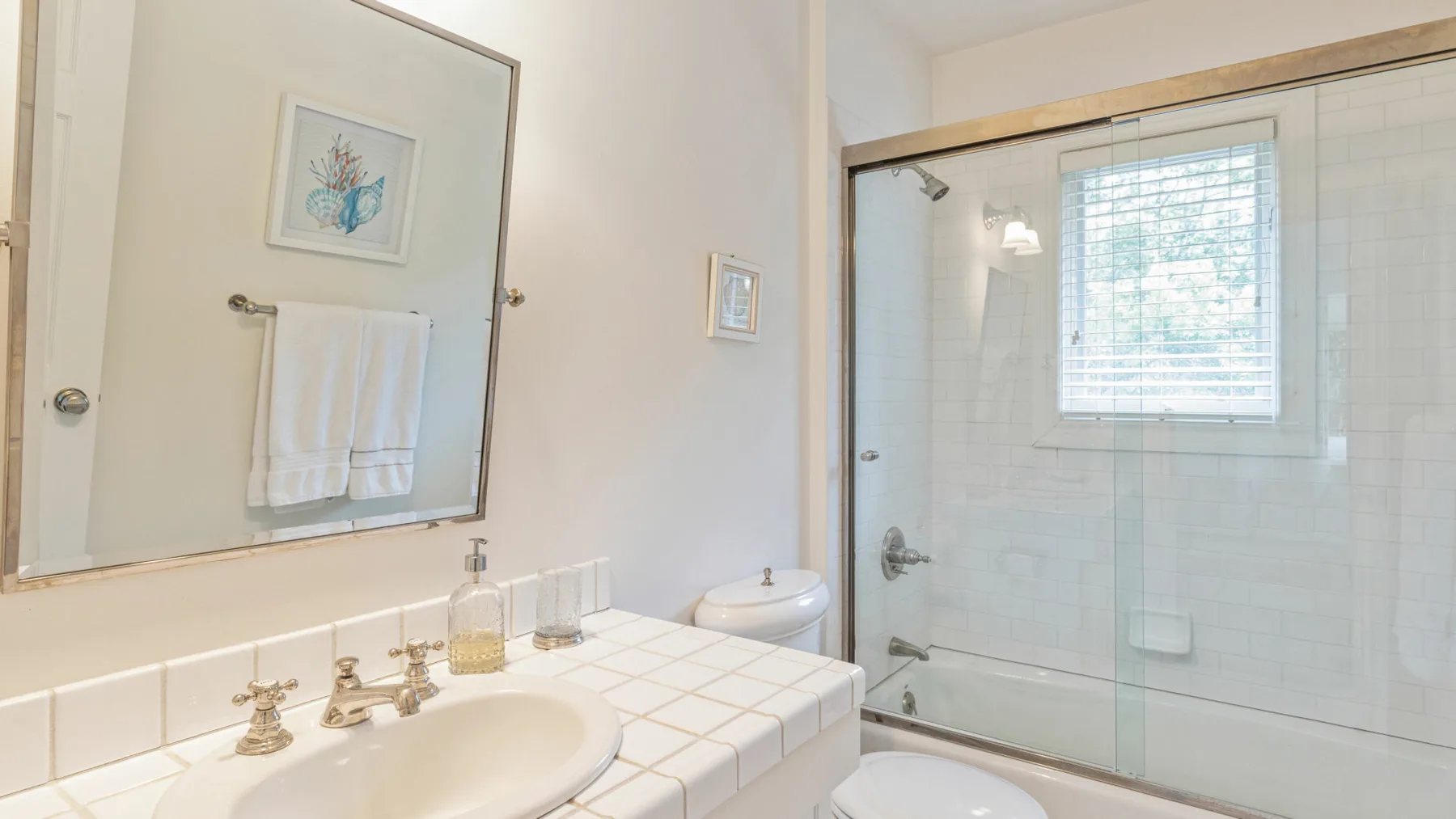 Un baño luminoso con lavabo alicatado y ducha de cristal.