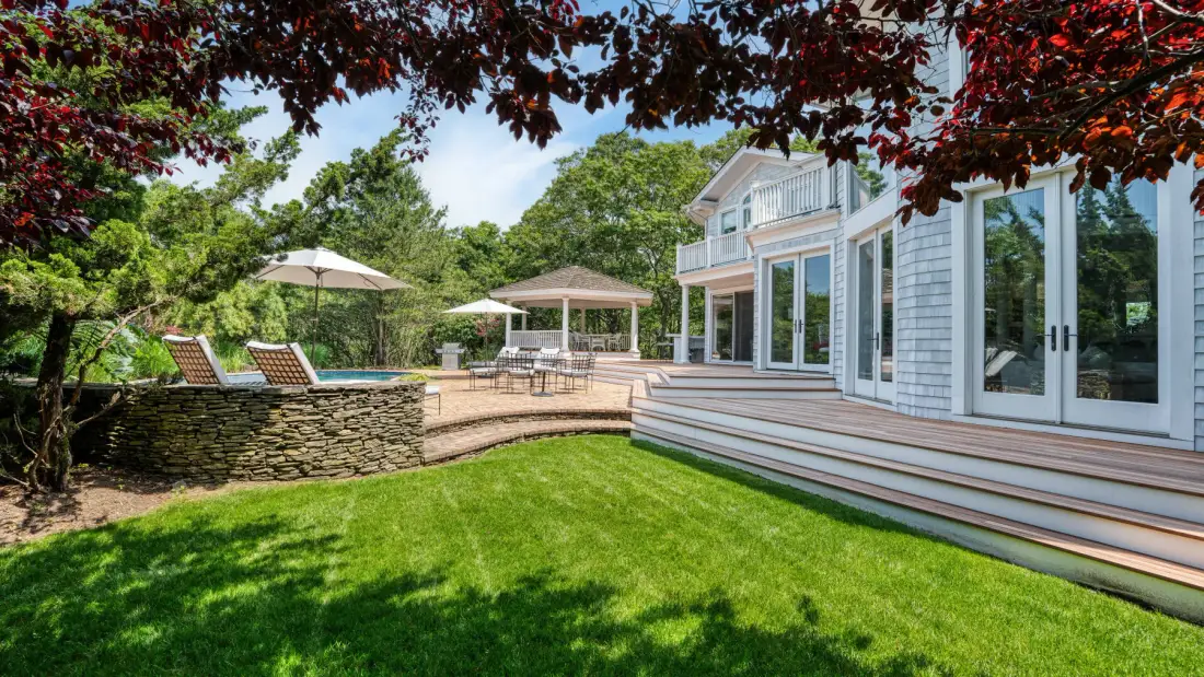 Un patio ajardinado con césped, asientos junto a la piscina y una casa blanca.