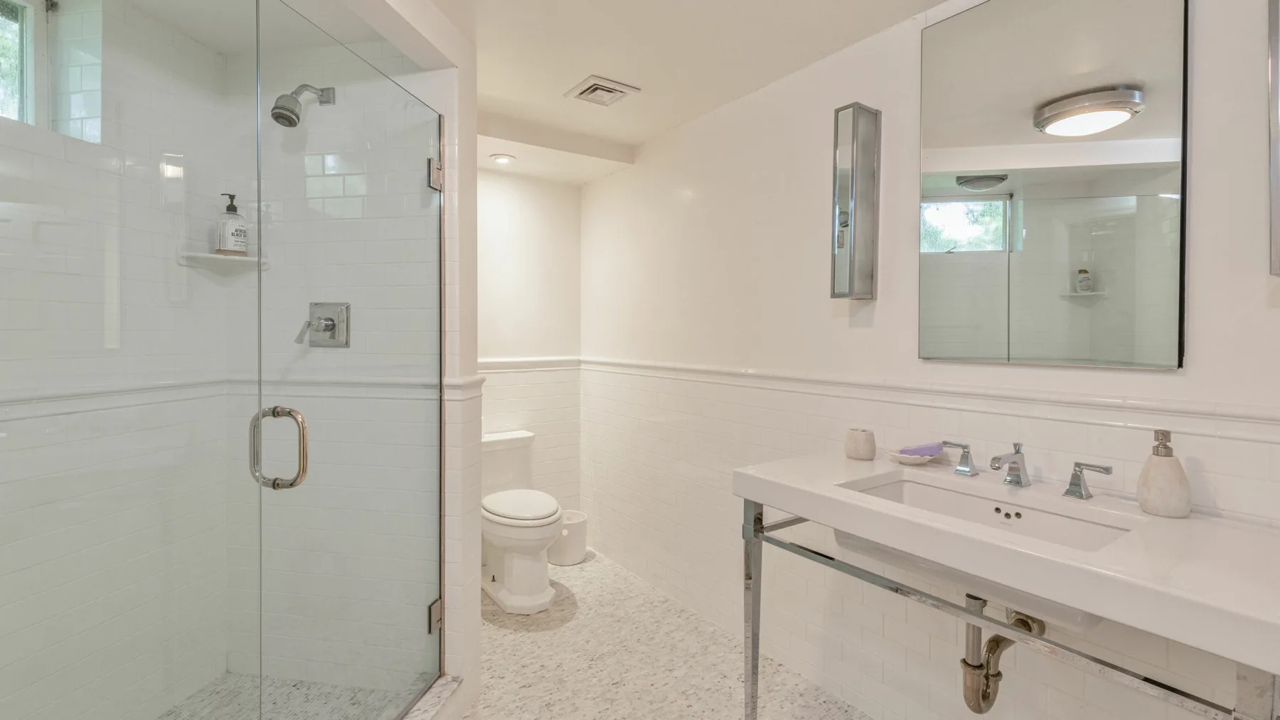 Un baño luminoso con ducha de vidrio, inodoro y una encimera larga con lavabo.