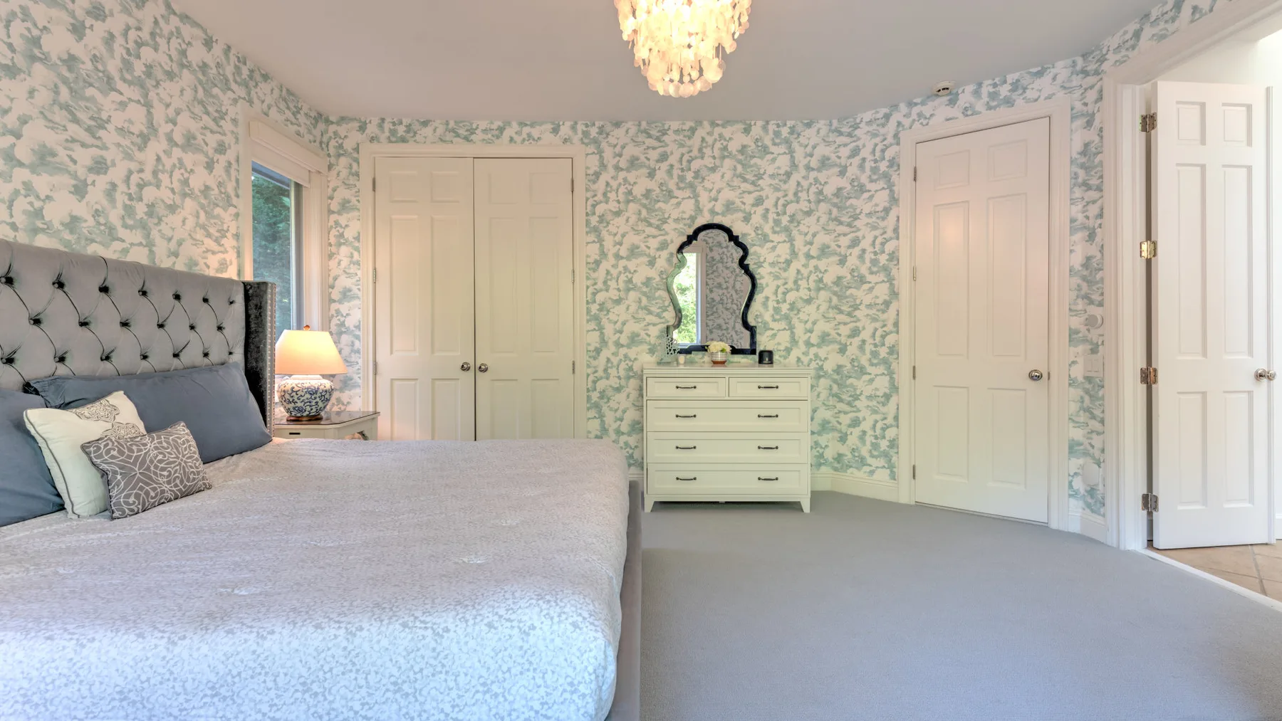 Un dormitorio con una cama, papel tapiz estampado y una cómoda con espejo.