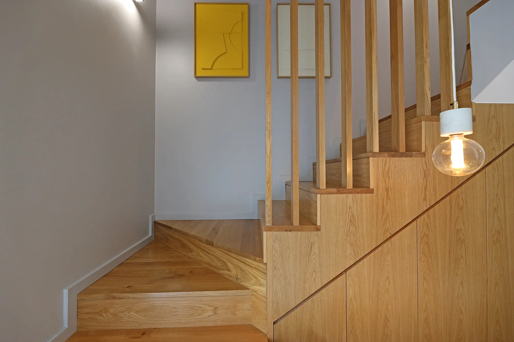A wooden staircase with vertical railings and framed artwork on the wall.