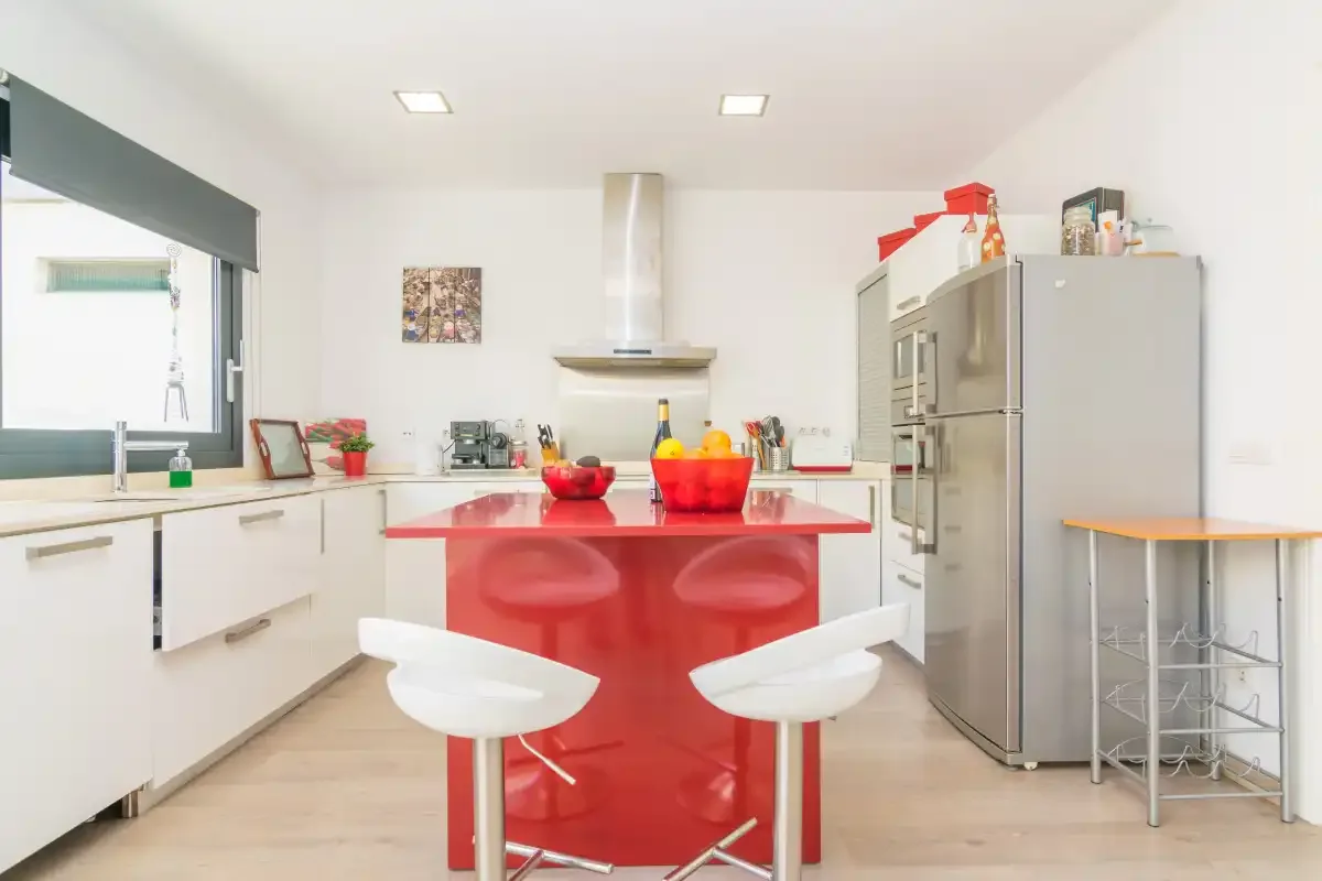 A bright kitchen with a red island and stainless steel appliances.