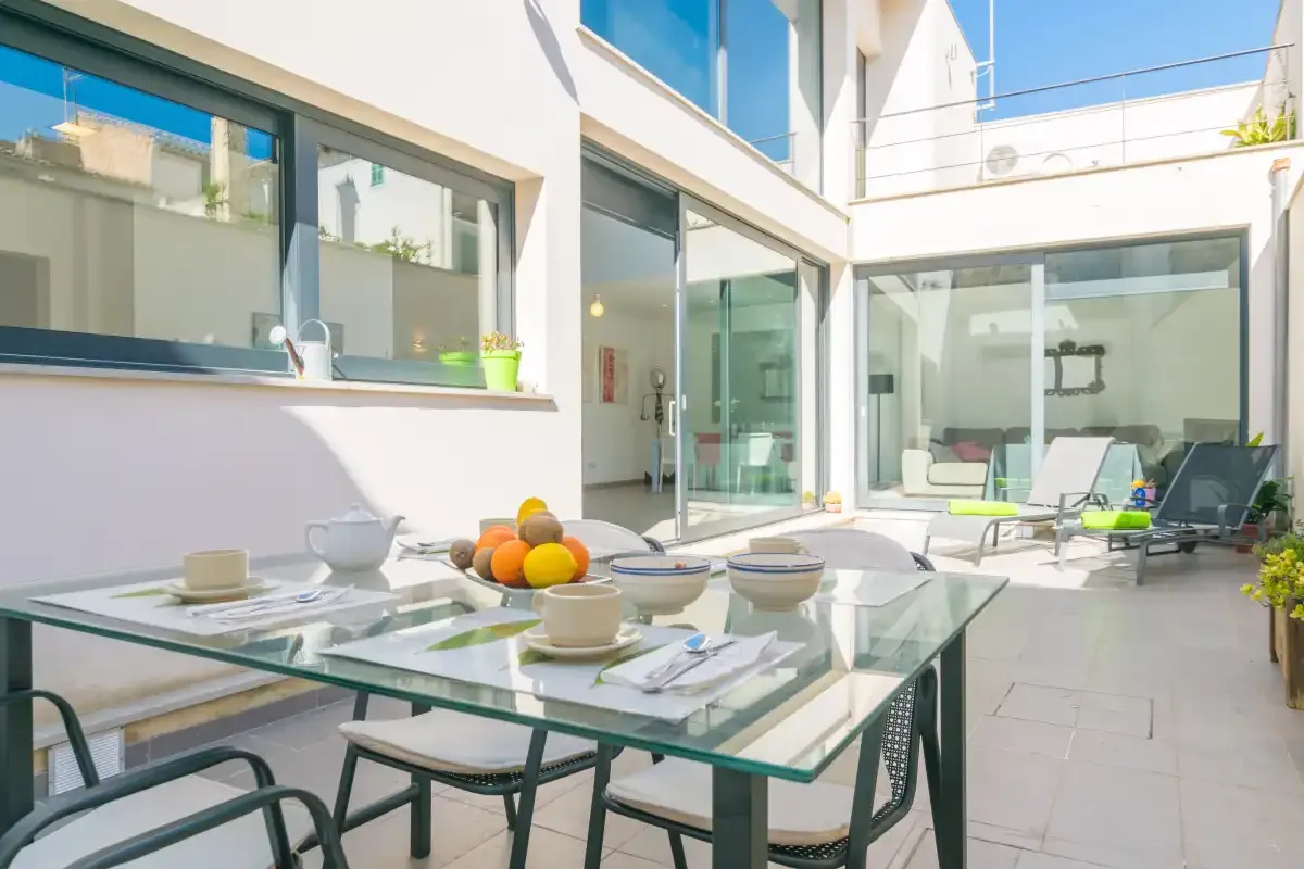A sunny courtyard dining area with a glass table and lounge seating.