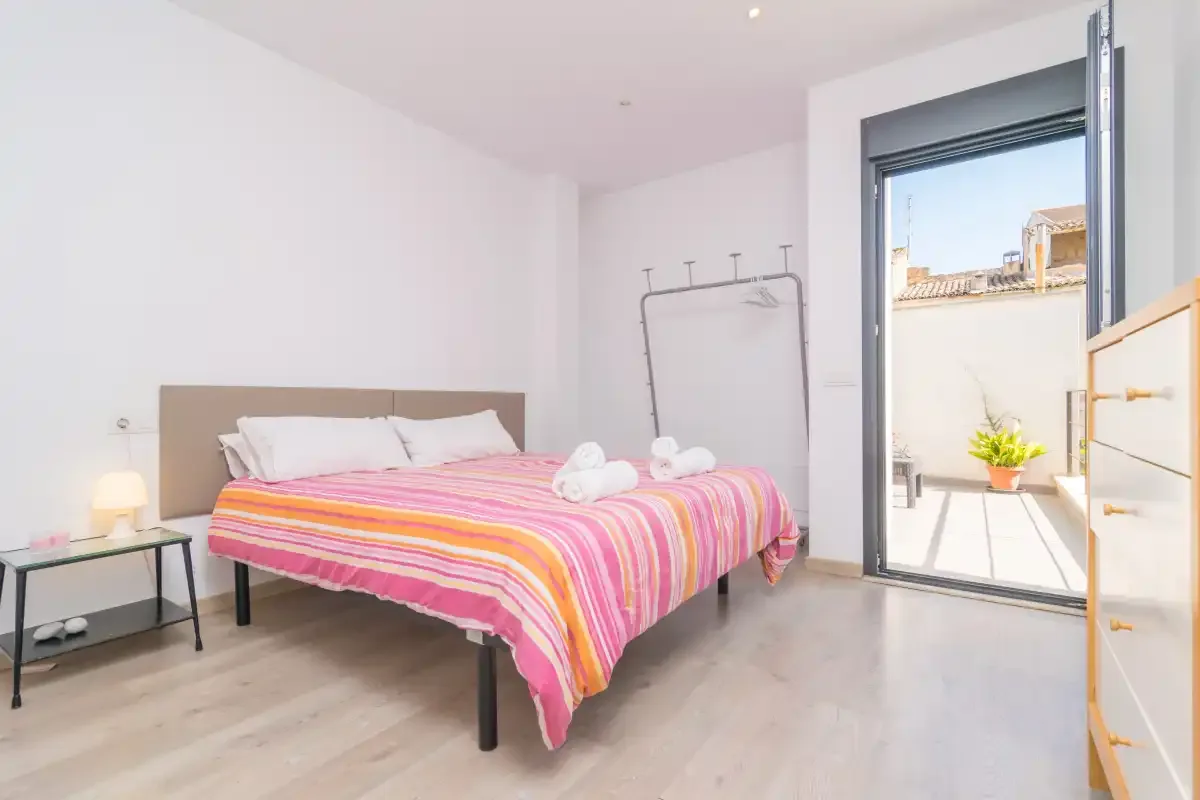 A bedroom with a colorful striped bedspread and an open balcony doorway.