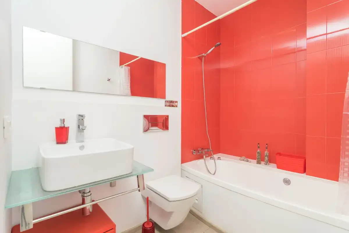 A bathroom with a glass shelf beneath a wide mirror and a bathtub.