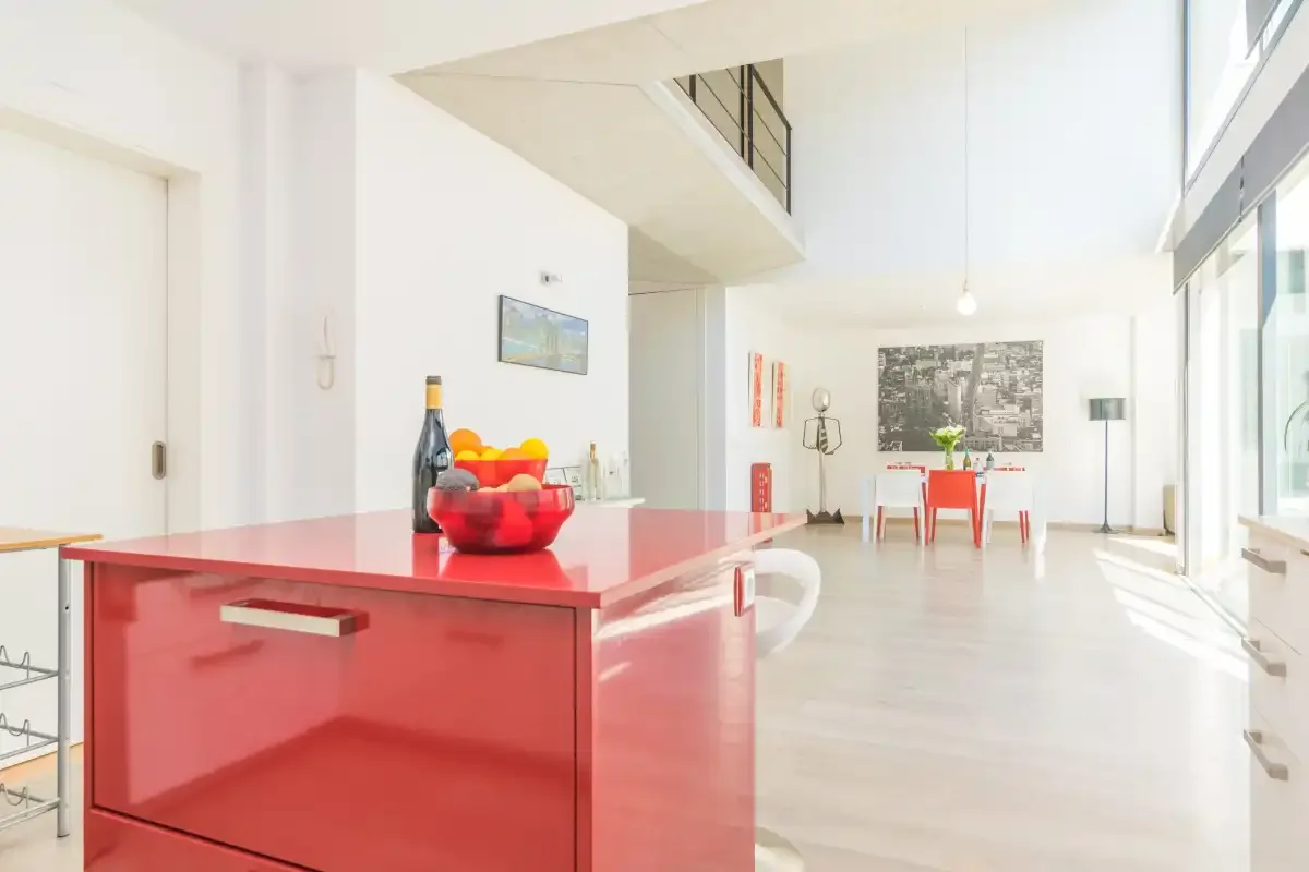 A bright open-plan kitchen and dining area with a red island and large windows.