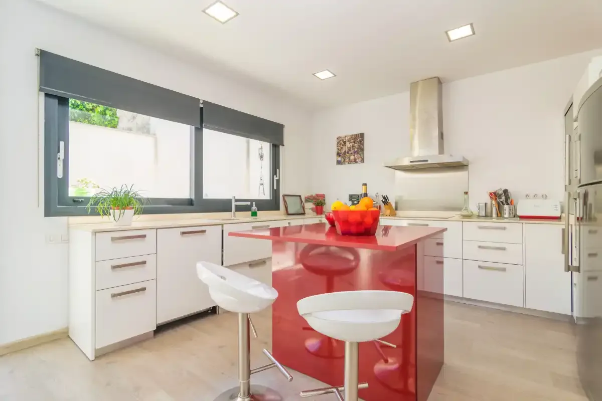 A bright kitchen with a red island and large windows.