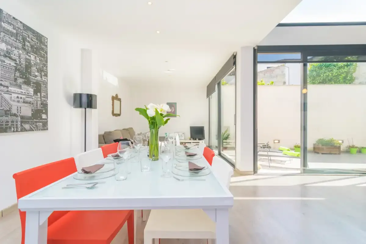 A bright dining area with a long table and red seating opens onto a patio.