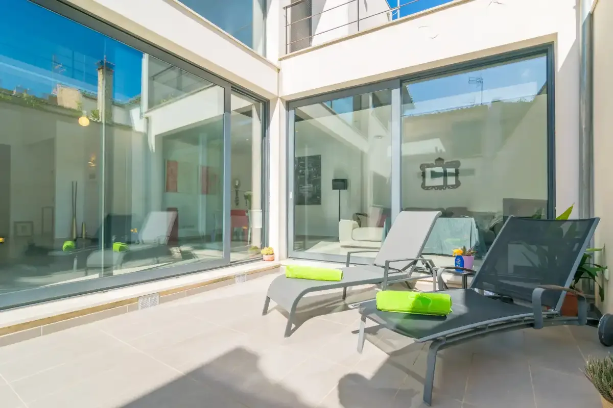 A sunlit patio with lounge seating beside large glass windows.